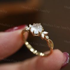 a close up of a person's hand holding a gold ring with a white stone