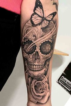 a woman's arm with a skull and rose tattoo on it, which has a butterfly flying over her head