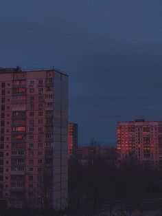 an apartment building lit up at night with the moon in the sky and buildings behind it