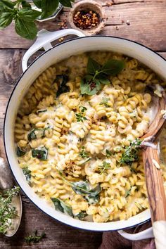 a pot filled with pasta and spinach on top of a wooden table next to a spoon