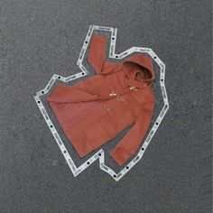 an orange jacket laying on the ground next to a pair of scissors and some tape