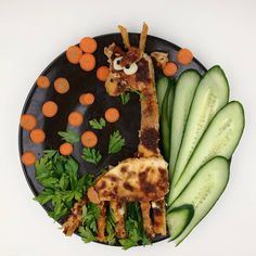 a black plate topped with cucumbers and carrots next to a giraffe cut in half