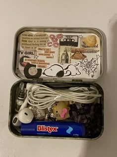 an open tin with various items in it on a white surface, including headphones and earbuds