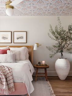 a bedroom with white bedding, pink pillows and a plant on the nightstand next to it