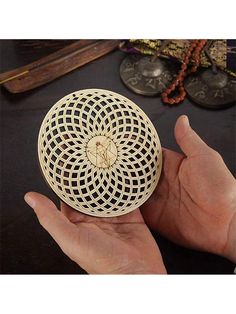 a hand holding a small wooden object in it's left hand with other items on the table behind it