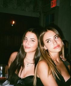 two beautiful young women sitting next to each other at a table with wine glasses on it