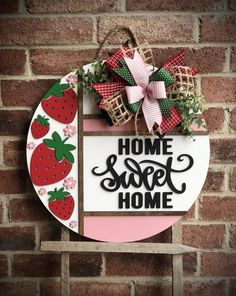 a sign that says home sweet home with strawberries hanging on the side of a brick wall