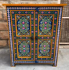 an ornately painted cabinet with flowers and leaves on the doors is sitting in front of a brick wall