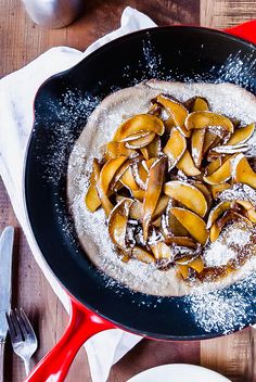 a skillet filled with powdered sugar and sliced apples on top of a wooden table