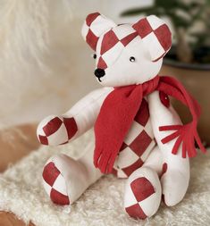 a red and white teddy bear with a scarf around it's neck sitting on a rug