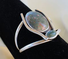 One-of-a-kind artistic hand-crafted sterling silver cuff bracelet set in a modernistic stylized design.  One large and one small natural ocean jasper cabochons in moss green with peach specks are the focal point of the design. Measurment: 5 1/2" with a 1 1/2" gap Sterling Silver Oval Cuff Bracelet, Unique Oval Gemstone Cuff Bracelet, Sterling Silver Cuff Bracelet, Metal Work, Sterling Silver Cuff, Ocean Jasper, Silver Cuff Bracelet, Silver Cuff, Moss Green