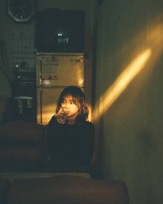 a woman sitting in the corner of a room with her hand on her mouth while looking at something