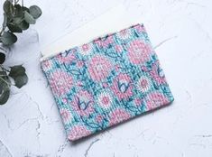 a pink and blue flowered pouch sitting on top of a white table next to a plant