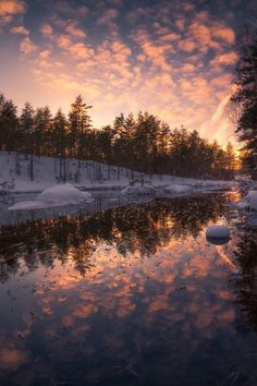 the sun is setting over a small lake with snow on the ground and trees in the background