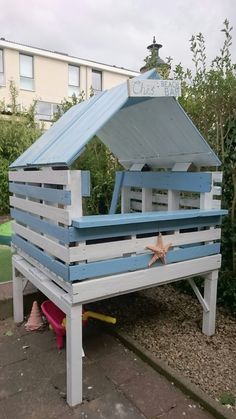 a blue and white wooden structure with a starfish on it's side in front of some bushes