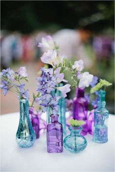 purple and blue vases with flowers in them on a white tableclothed surface