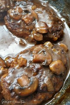 two meat patties covered in mushroom gravy on top of a frying pan