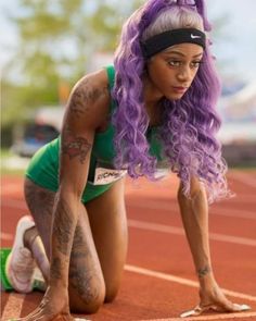 a woman with purple hair is kneeling on a track