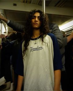 a man with long curly hair standing on a subway train holding his arm up in the air