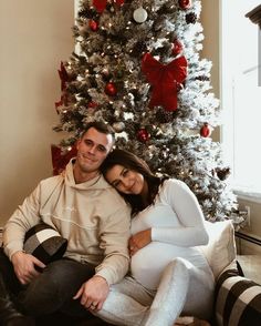 a man and woman sitting in front of a christmas tree