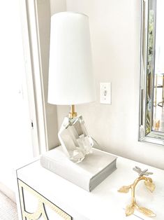 a white lamp sitting on top of a table next to a book and a mirror