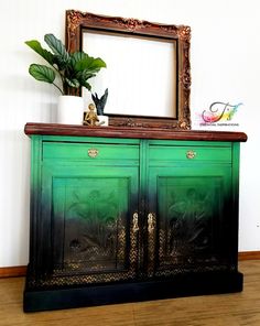 a green and black painted dresser with a mirror on it's top, next to a potted plant