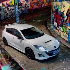 a white car parked in front of graffiti covered walls