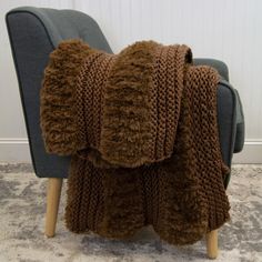 a brown blanket sitting on top of a chair next to a gray chair and white wall