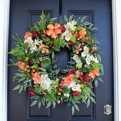 a wreath on the front door with flowers and greenery hanging from it's sides