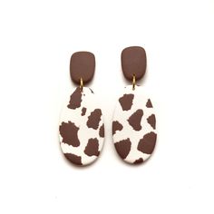 the brown and white cow print earrings are hanging from gold earwires on a white background