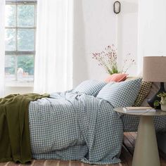 a bed with blue and white checkered comforter next to a lamp on a table