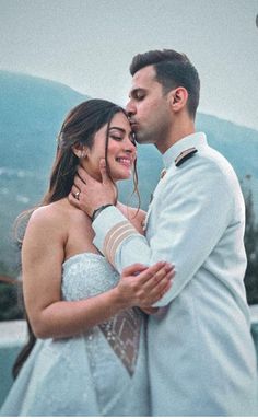 a man and woman standing next to each other in front of a pool with mountains behind them