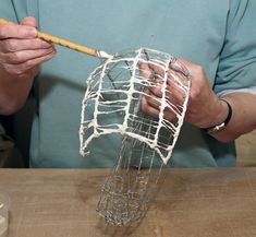 a man is making a sculpture out of wire on a wooden table with a stick