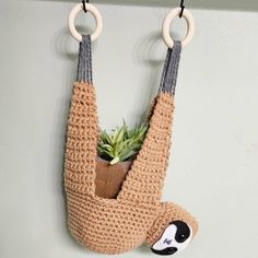 a crocheted sloth hanging on a wall with a plant in it's mouth