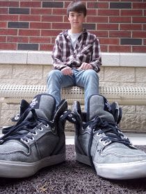 a man sitting on top of a white bench next to a brick wall and wearing sneakers