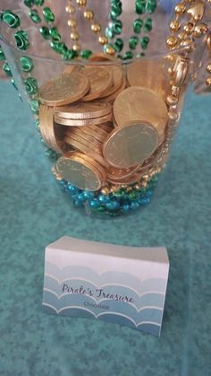 a glass bowl filled with gold coins and green beads next to a business card on a table