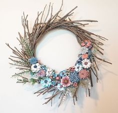 a wreath made out of twigs with flowers and leaves on it's sides is hanging on the wall