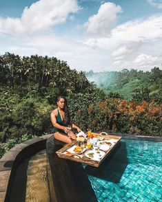 a woman sitting at a table with food on it in the middle of a pool