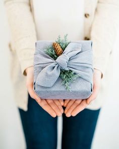 a person holding a wrapped present with a pine cone on it's top and ribbon