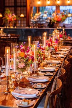 a long table is set with candles and flowers in vases, plates and silverware