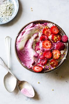 a bowl filled with ice cream and strawberries on top of a white table next to two spoons