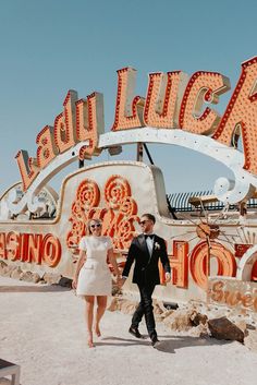 a man and woman walking in front of a neon sign