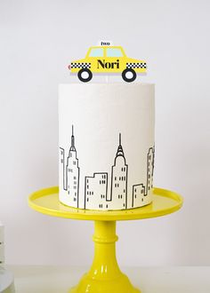 a yellow cake sitting on top of a yellow plate next to a cupcake with a city scene on it