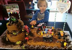 a young boy sitting in front of a birthday cake with monster trucks on the top