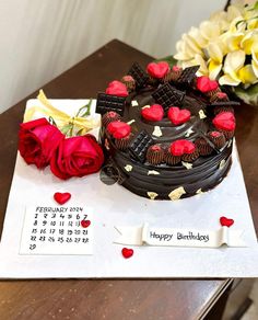 a chocolate birthday cake with red roses on the table next to it and a calendar