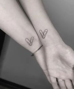 two people holding hands with tattoos on their arms and one has a heart in the middle