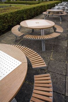 several wooden benches are lined up on the sidewalk near bushes and hedges in front of a building