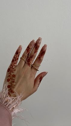 a woman's hand with hennap and rings on her left hand, against a white wall