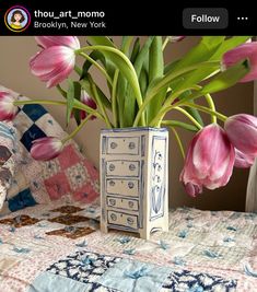 pink tulips are in a vase on a quilted bedspread, with the words thou art mom below it