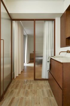 an open door leading to a bathroom with wood floors and white drapes on the sliding glass doors